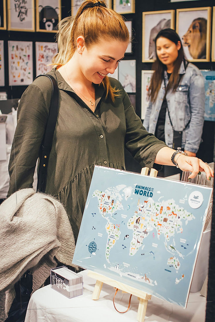 Woman looking at an Animals world map nursery and kids wall art print on an easel in an art gallery - Bluish Nest Art Studio