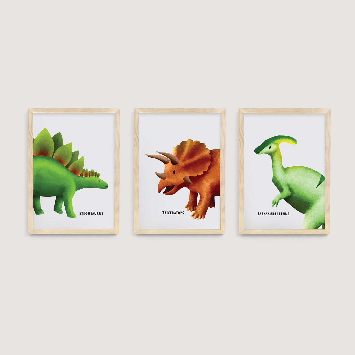 Three framed nursery prints of stegosaurus, triceratops and Parasaurolophus dinosaurs on a white wall  - Bluish Nest Art Studio