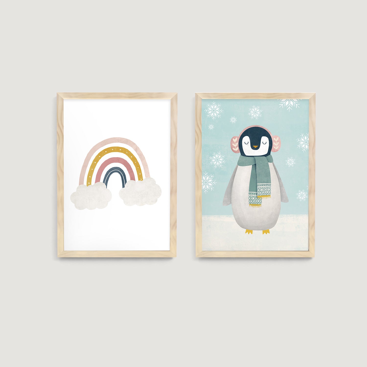 Two framed children and baby wall art prints on a wall, one with a rainbow and clouds, the other with a penguin in a scarf  - Bluish Nest Art Studio