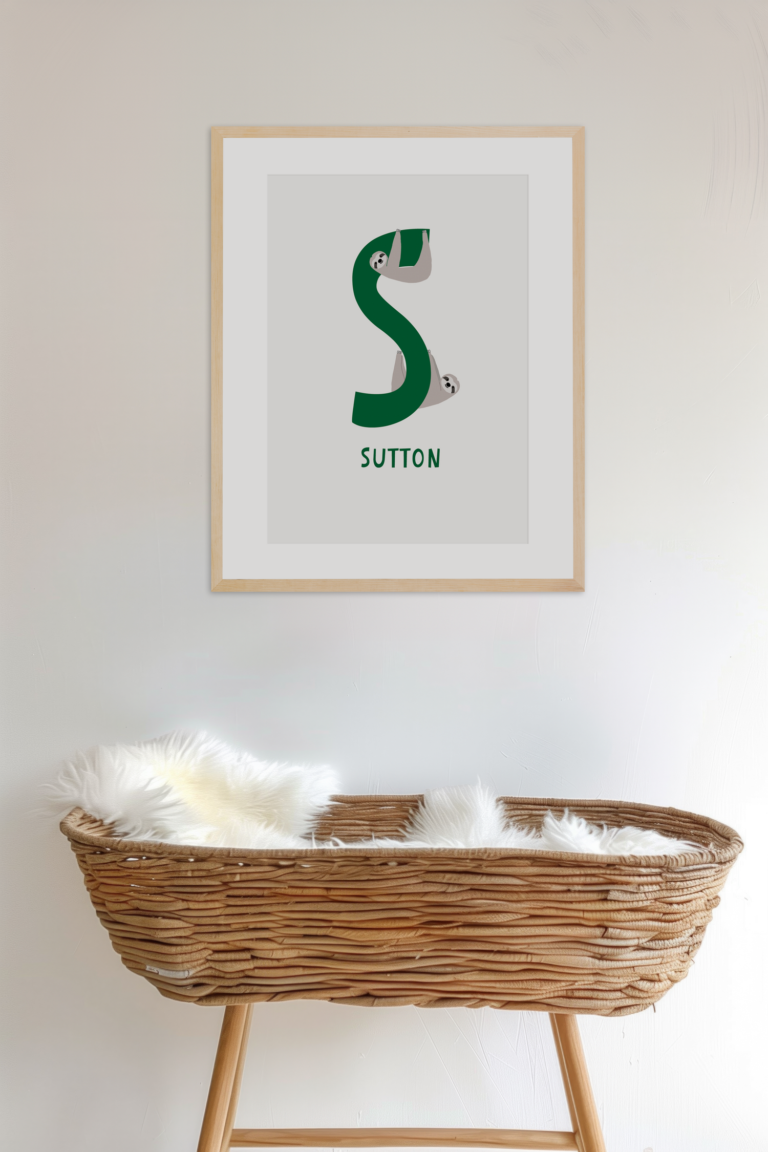 Personalised name and letter nursery framed print a green letter 'S', with name Sutton and illustration of two sloths, hanging above a wicker crib in a nursery room - Bluish Nest Art Studio