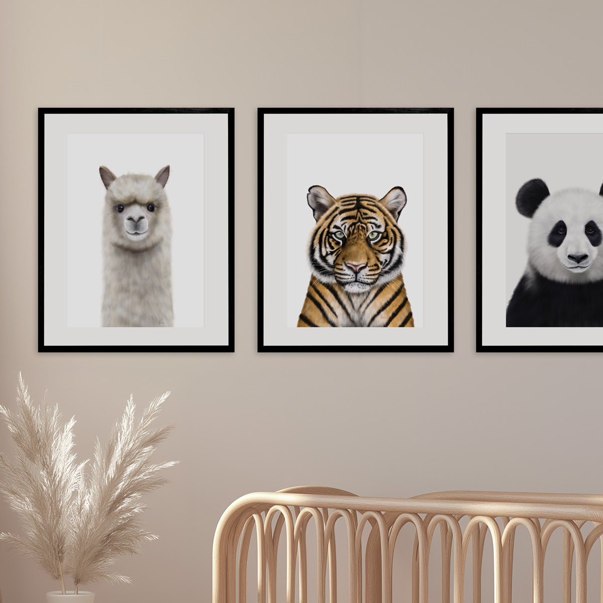 Three framed animal kids and baby art prints of an alpaca, tiger and panda on a wall with a decorative plant and chair in the foreground, in a nursery  room - Bluish Nest Art Studio